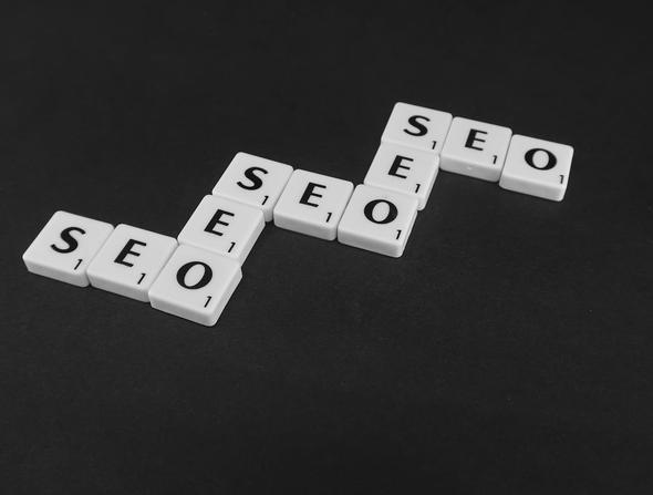 This conceptual image features white letter tiles arranged on a black surface, spelling "SEO" three times in an ascending diagonal pattern, visually representing the layered search engine optimization strategies discussed in the article. The staircase arrangement symbolizes the progressive steps property managers must take — from Vrbo platform optimization to on-page website SEO to technical SEO — to climb search rankings on both Vrbo's internal algorithm and Google Search results