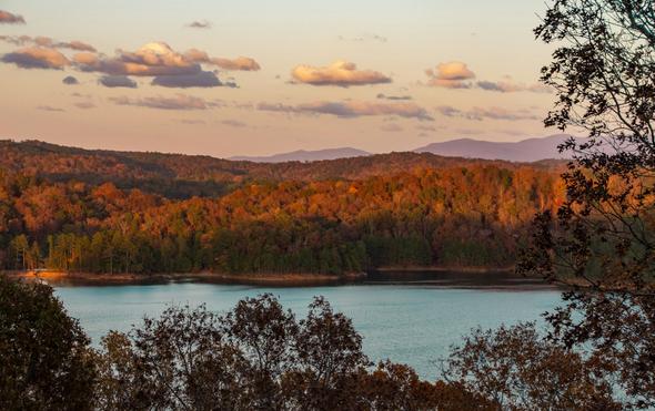Autumn landscape in Sandy Springs, Georgia, featuring vibrant fall foliage, a serene lake, and distant mountain views under a soft sunset sky.