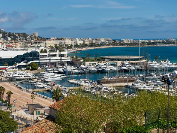 A vibrant view of the Cannes harbor, filled with luxury yachts, set against the backdrop of the city and the sparkling blue Mediterranean Sea.