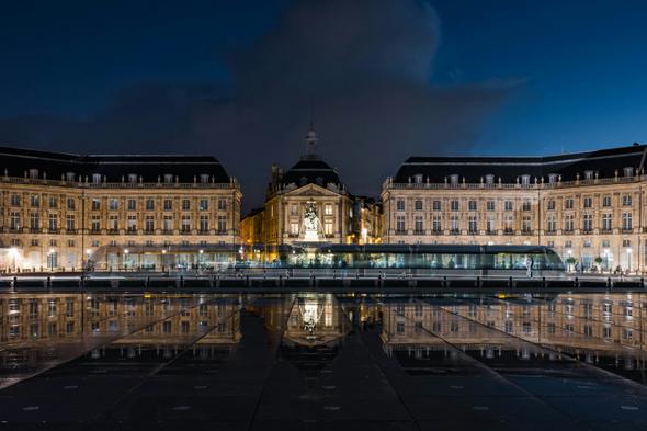 An image of the majestic Place de la Bourse in Bordeaux at night, its reflection mirrored perfectly in the iconic Miroir d’Eau.