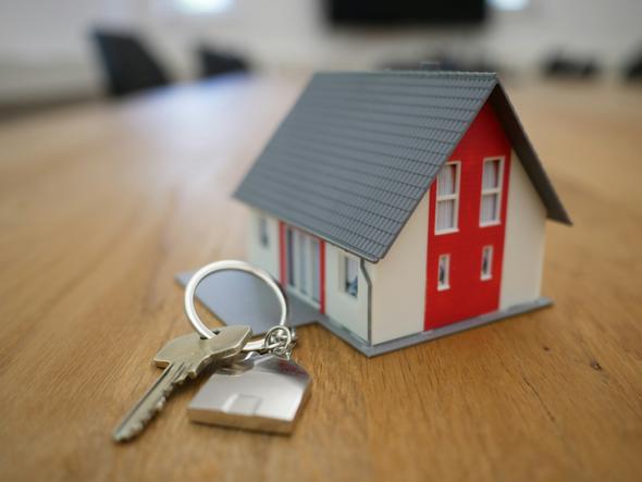 A symbolic representation of homeownership and property management, featuring a miniature house model and keys on a wooden surface. 
